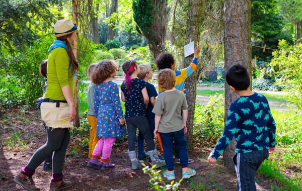 Eine Kindergruppe_hängt Infos zum Thema Stadtnatur zwischen zwei Bäumen auf. Sie werden von einer Naturpädagoin begleitet.